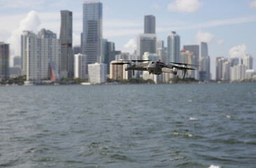 Fototapeta na wymiar drone or quadcopter in flight against the background of city skyscrapers and water of the sea or river. New technology concept. Panorama of the city.