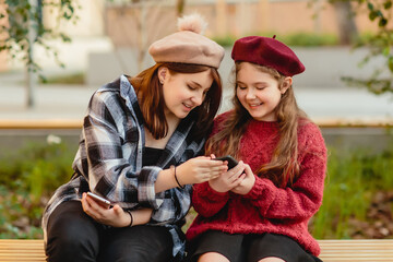 Two laughing schoolgirls, a teenager and a child in school uniform and berets look into a mobile device.