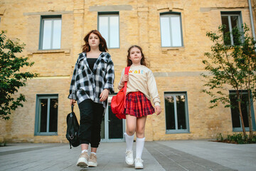 Back to school concept. Two schoolgirls in uniform with backpacks against the school background.