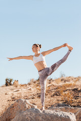 Fit woman in white top practicing yoga in desert on sunny day, health and active life concept