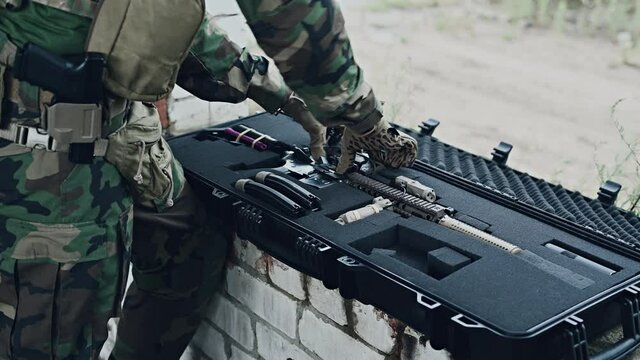 The soldier pulls a rifle out of the ammunition case and insert ammunition clip into assault rifle