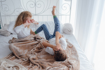 High angle of little sister and brother in pajamas awakening in cozy bed in light bedroom in morning