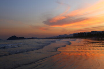 Fototapeta na wymiar Ocean with calm waves on the shore during a beautiful red sunset. Bertioga, city, Brazil