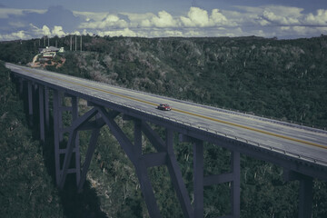 Fototapeta na wymiar Vehículo antiguo cruza el puente sobre el bosque. Puente de autopista con un vehículo rojo solitario. Cuba. 