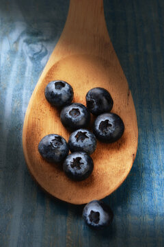 Closeup of fresh blueberries on a wooden spoon laying on a rustic painted farmhouse style kitchen table with warm side light.