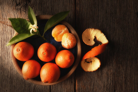 Closeup of still life of Minneola Tangelos on a plate with leaves and orange blossom on a rustic wood table, and warm side light.