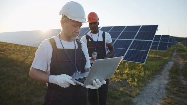 Couple of mixed race engineers working at solar power plant and using laptop computer for maintenance. Teamwork. Innovation. Industry.