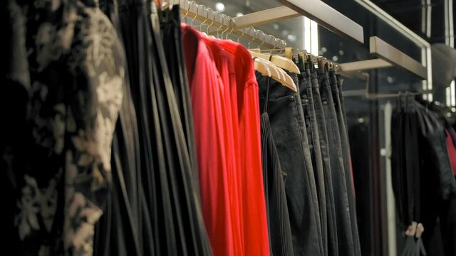 Hangers with dresses, pants and shirts in the clothing store. Slow motion handheld shot.