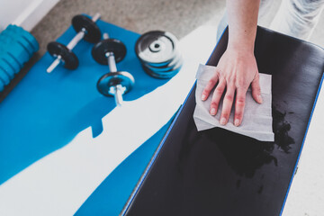 the new normal after covid-19, hand cleaning gym equipment with disinfectant wipe against virus and bacteria