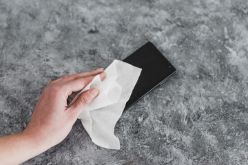 the new normal after covid-19,  hand cleaning smartphone with disinfectant wipe to flatten the curve and prevent viruses and bacteria