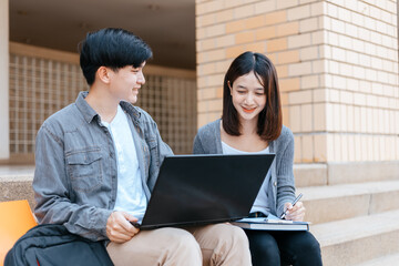  teenager sitting on stair at college campus with school books and a laptop computer doing homework. Education concept.