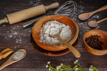 flour, sugar and chocolate granules for preparation of making bread on Indonesian traditional cutlery set or tableware made of wood isolated on brown