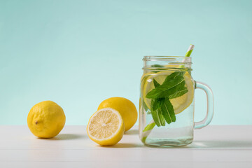 A large mug of cold water with lemon and mint on a white table on a blue background.