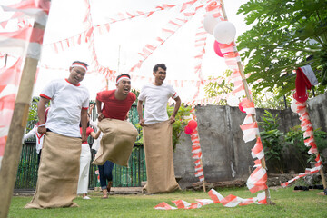 three young men happily joined in sack race jumping quickly to reach the finish line in the...