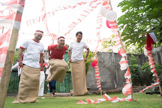 three young men happily joined in sack race jumping quickly to reach the finish line in the celebration of August 17 Indonesian Independence Day