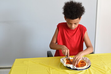 Mixed boy cut and eat pepperoni pizza at home. Kids and food. School boy eating lunch