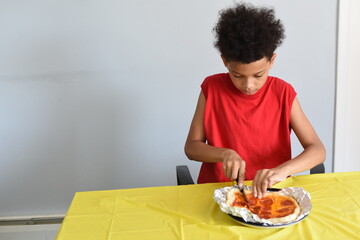 Mixed boy cut and eat pepperoni pizza at home. Kids and food. School boy eating lunch