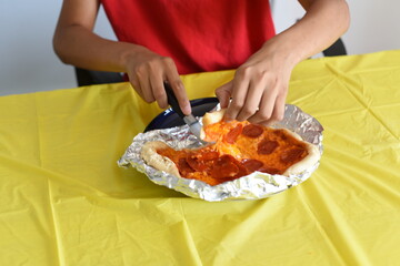 Mixed boy cut and eat pepperoni pizza at home. Kids and food. School boy eating lunch