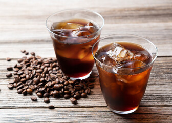 Cold coffee in a glass with coffee beans behind it.