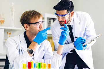 Professional two scientist man research and working doing a chemical experiment while making analyzing and mixing  liquid in test tube.Young science man dropping sample chemical on glass at laboratory