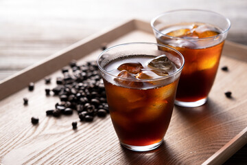 Cold coffee in a glass with coffee beans behind it.