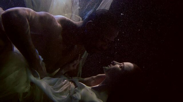 white woman and black man underwater, embracing and looking to each other