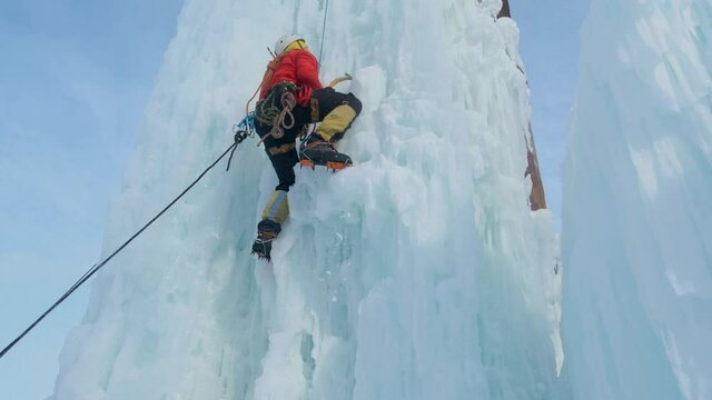 Alpinist man with ice tools axe climbing a large wall of ice.