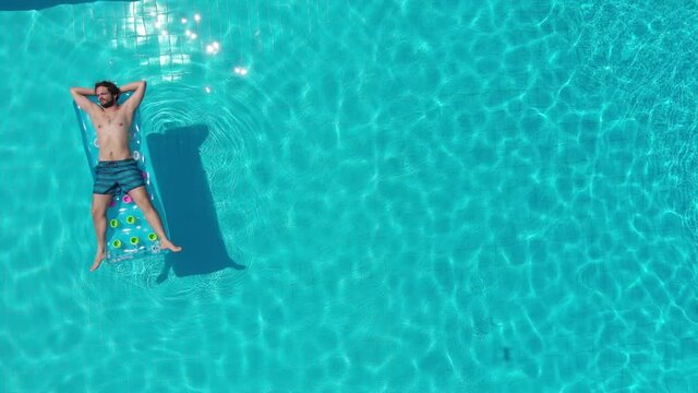 aerial view of young man lying on the mattress in the blue water of the pool