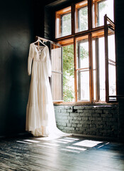 Elegant wedding dress hanging on window. Wedding morning