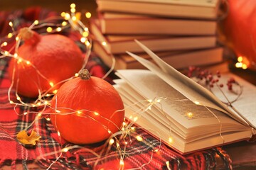 Autumn books.Autumn cozy reading.Stack of books, red hokkaido pumpkins with glowing garland, checkered scarf close-up on a wooden table.NaNoWriMo Writing Autumn Marathon