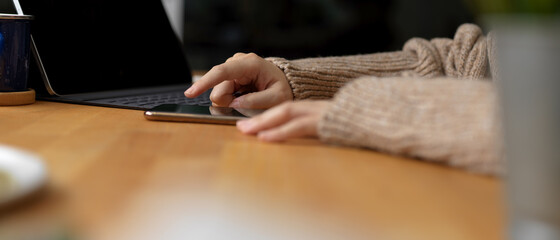 Female touching on smartphone while sitting at workspace with digital tablet and copy space on wooden table