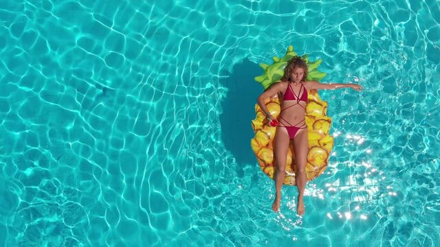 overhead shot of young woman in the poll lying on the pineapple-shaped mattress 