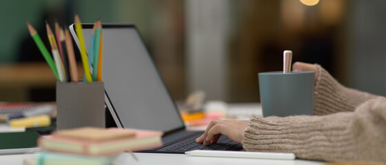 Female student doing assignment with mock up tablet while holding cup on study table