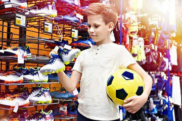Boy with ball and boots in football sport store