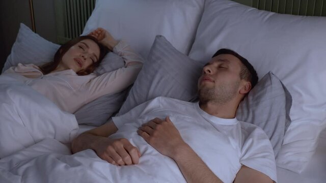 Young irritated man reading newspaper because of snoring wife in bed