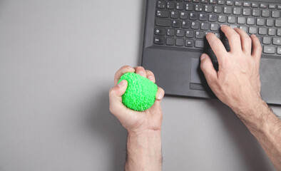 Man squeezing stress ball while working with laptop.