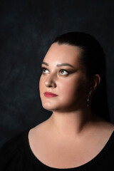 portrait of a beautiful girl of normal build on a dark background close-up. The brunette looks to...
