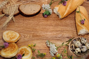 still life of homemade rustic products in the form of a frame Quail eggs bread pumpkin pancakes wheat ears and wild flowers on a wood background