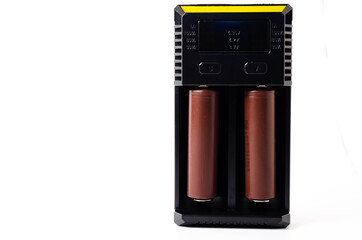 A black charger for two 18650 batteries. A green and brown 18650 battery on a white background next to the discharge, on charging. Male hand puts the battery on charge