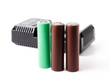 A black charger for two 18650 batteries. A green and brown 18650 battery on a white background next to the discharge, on charging. Male hand puts the battery on charge