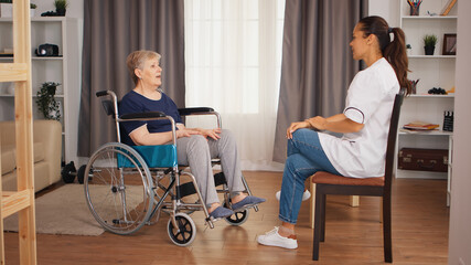 Handicapped senior woman in wheelchair talking with female nurse. Old person retirement home, healthcare nursing, health support, social assistance, doctor and home service