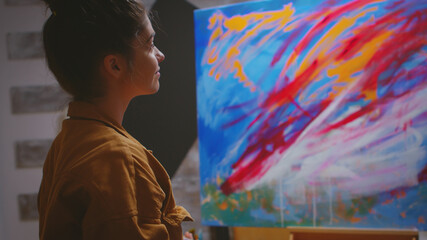 Creative pensive painter in workshop admiring her work.