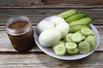 Fresh whole cucumber, pile of cutting cucumber and boiled chicken eggs on the plate with tamarind paste in the plastic package. Famous spicy and healthy menu in Thailand. Vegetable with Chilly sauce.