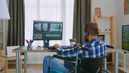 Handicapped video editor in wheelchair working from home wearing headphones.