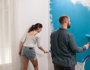 Fototapeta premium Apartment wall painted with blue by two young artists. Home during renovation, decoration and painting. Interior apartment improvement maintenance. Roller, ladder for house repair