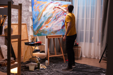 Talented young man painting on large canvas in studio. Modern artwork paint on canvas, creative, contemporary and successful fine art artist drawing masterpiece