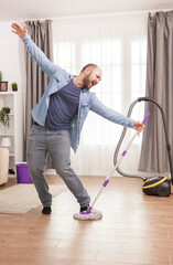 Cheerful man dancing with mop while cleaning the floor.