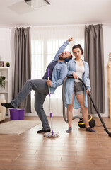 Husband having fun while wife is cleaning the floor with vacuum cleaner.