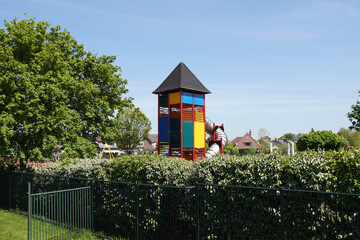 Dutch playground in Holland. A colorful climbing tower and slide behind a hedge and fence in spring.