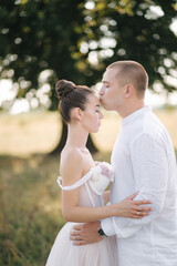 Close up portrait of groom kiss bride in forehead in front of big tree. Side view